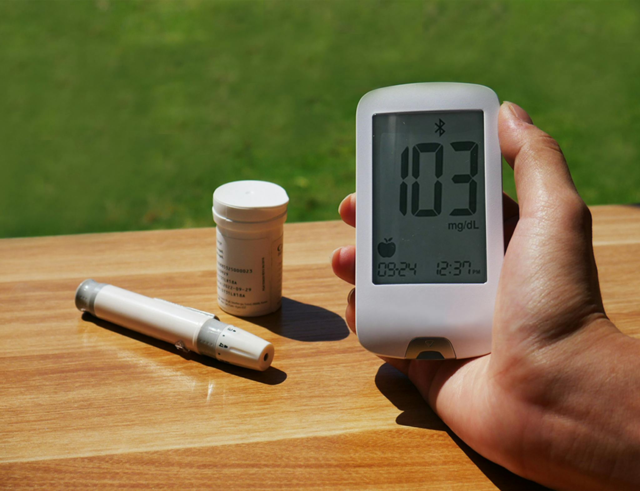 Blood glucose monitor displaying 103 mg/dL outdoors, emphasizing diabetes care.